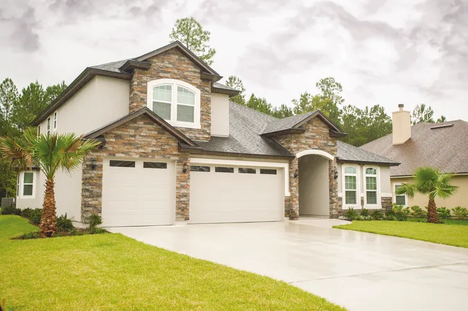 Gray long panel garage door with clear windows installed on a two-story stone home
