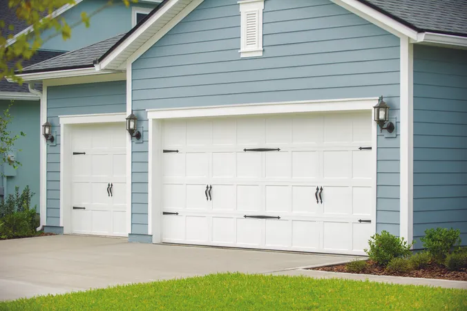 White short panel garage door with no windows and decorative hardware installed on ranch home with baby blue siding 