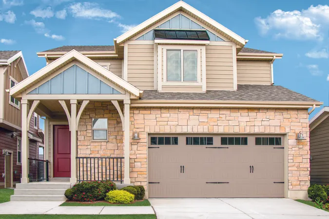 Taupe colored vertical short panel garage door with stockbridge windows and decorative hardware on a two-story home